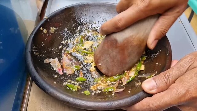 chef preparing food. Close-up of street vendor hand grinding chili, garlic and spices in wooden mortar and pestle to make traditional sambal for Tahu Gejrot. Authentic street food preparation