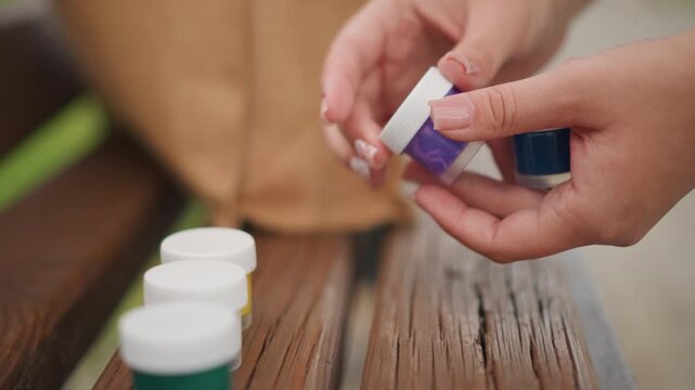 Choosing vibrant paint jars. Outdoor scene of person choosing tiny colorful paint boxes carefully. Closeup photograph showing someone carefully selecting miniature vivid paint containers outdoors