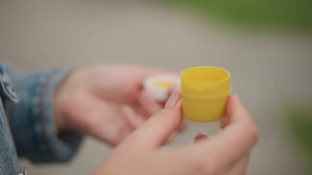 Urban closeup hands opening balm jar, denim jacket on street bench, white lid removal reveals yellow container, tester swipe hints of cream, quick onthego skincare routine for natural glow