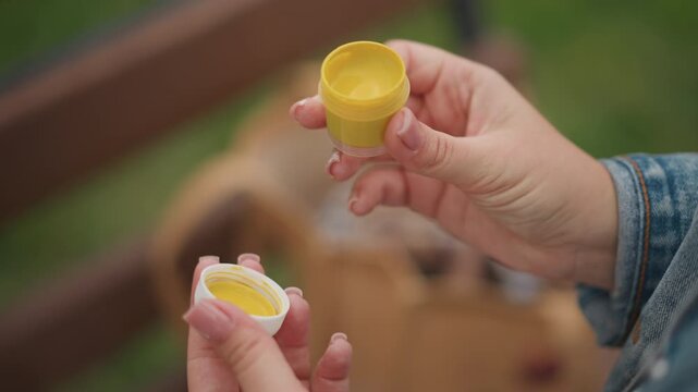 Park bench closeup hands opening container, careful inspection of sterile yellow specimen jar, removing white lid and examining interior for residue, preparing sample for clinic dropoff with focused