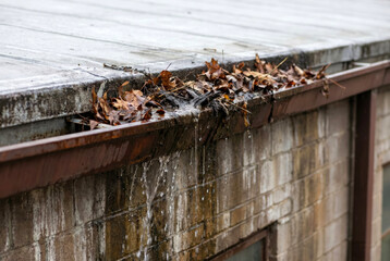Overflowing blocked gutter with leaves and debris, water cascading over edge, drainage failure concept