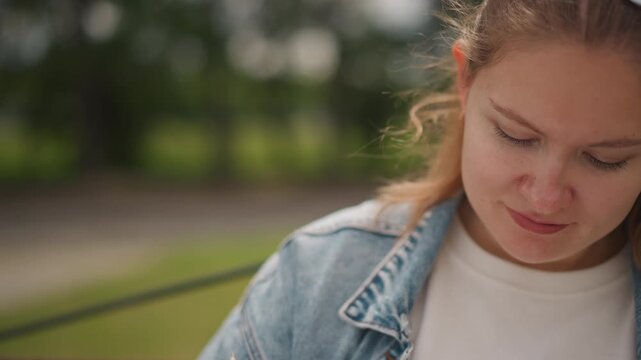 Silent reflective woman. Introspective woman gazing down thoughtfully. Contemplative woman in denim jacket with vape outdoors. Serene woman appears lost in thought on park bench during daylight