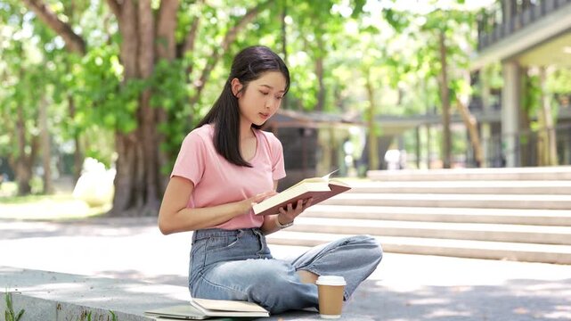 Female student sitting outdoor, reading book, studying for final exam at university.