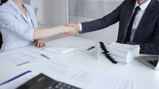 Business partners sealing a deal with a handshake over documents and a calculator on an office desk, teamwork and trust. Audit and taxes