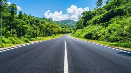 Fototapeta premium Asphalt road stretches into distance, lined with vibrant green forest under a bright blue sky