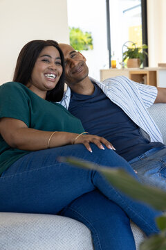 African American couple sitting closely on light-colored sofa in bright living room with plants
