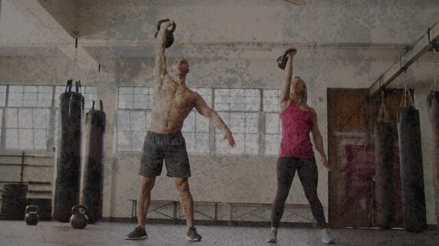Man and woman in gym holding kettlebells overhead then hinging, rotating and lowering hand for core