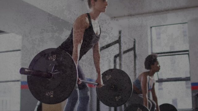 Two women driving hips and lifting barbells in gym, strength-training with squat rack and plates