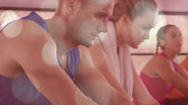 Man and woman riding spin bikes on instructor cue for fitness, towel dabbing, pink bokeh overlaying