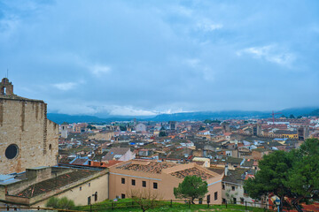 Fototapeta premium Panoramic view of the Catalan town of Montblanc (Spain), with rooftops and mountains in the distance, on a cloudy day. On the left the church of Santa Maria. 