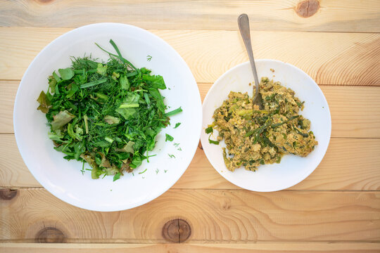 Fresh wild herbs and scrambled eggs on wooden table. Healthy organic breakfast with green leeks and herbs served in white bowls for rustic dining concept