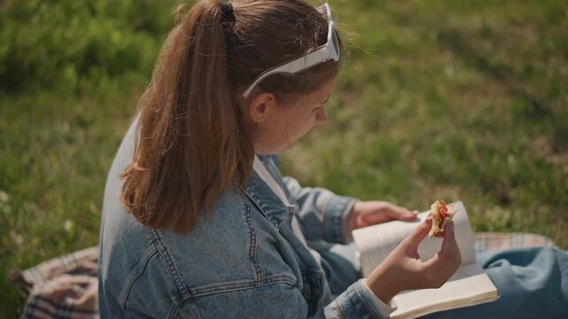 Peaceful park reading. Student leisurely studies outdoors today. Relaxed individual enjoying peaceful time with book outside. Serene moment of studying and relaxing on sunny grassy park blanket