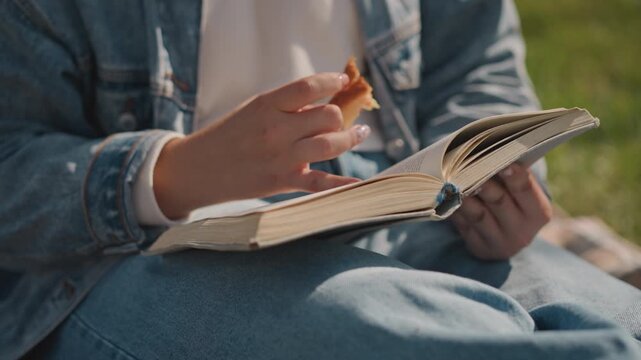Caucasian reader flipping book pages while nibbling pastry on denim lap, soft sunlight over grassy picnic, closeup hands turning textured notebook pages, cozy slow living mood, student and writer