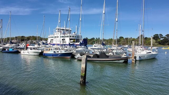 Lymington Hampshire England UK. Video. An Isle of Wight  passenger and vehicle ferry on the Lymington river bound for the IOW passing small boats on pontoone in mid stream.