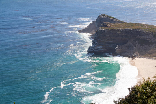 Coastal rocky cliff overlooking blue ocean. High angle aerial view showing turquoise waves and sandy beach for nature travel tourism landscape