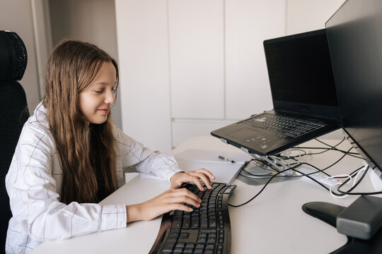 Young girl concentrating as she types code on keyboard at multi screen desk, engaged in online learning and developing digital skills for future tech and education careers.