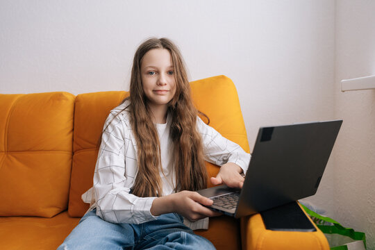 Young female student engaging in online learning, sitting comfortably on an orange sofa at home, creating modern education and digital lifestyle concept.