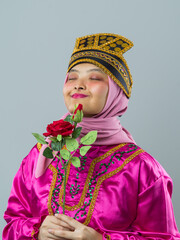 Naklejka premium Smiling Young Indonesian Asian Woman In Pink Hijab And Traditional Gold-Trimmed Costume Holding A Red Rose