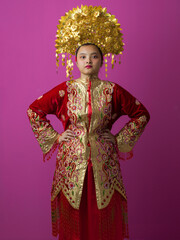 Naklejka premium Young Indonesian Asian Woman In Traditional Red And Gold Chinese Wedding Costume With Ornate Golden Headdress