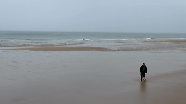 Walking a dog on Omaha Beach during a cloudy day with ocean waves in the background