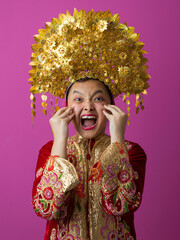Naklejka premium Excited Indonesian Asian Girl Wearing Traditional Gold Headdress and Embroidered Red Costume Celebrating Festival