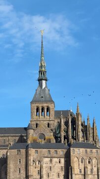 Explore the stunning architecture of Mont Saint-Michel in Normandy with a view of its tall spire and historic buildings