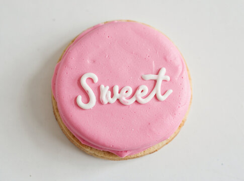 A single pink frosted cookie with the word 'sweet' written on it in cursive script