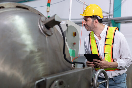 Worker stands in a factory with machinery while holding a tablet in hand