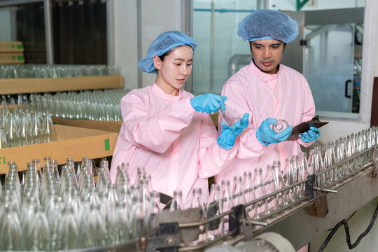 Workers examine bottles in a factory while recording data during quality control checks