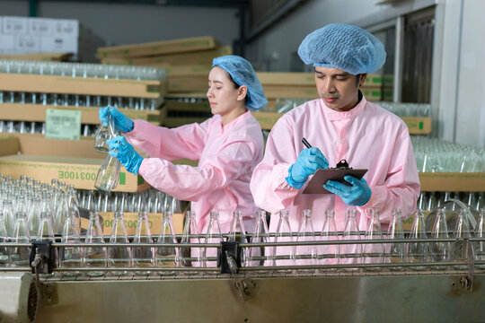 Workers examine bottles in a factory while recording data during quality control checks