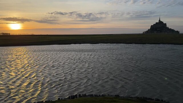 Sunset over Mont Saint Michel in Normandy with calm water and distant landscape
