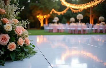 Naklejka premium Elegant wedding reception setup with floral arrangements and string lights. Outdoor dance floor and tables await guests for a festive celebration under warm illumination.