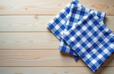 Obraz premium Two blue, white checkered napkins lay on light wooden table. This simple pattern evokes rustic, traditional German setting, perfect for festive occasions, culinary themes. Clean, inviting surface.