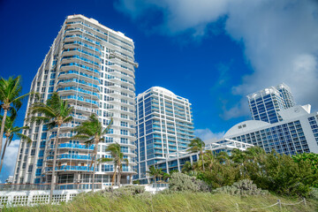 Obraz premium Modern Miami Beach waterfront high-rise condominiums and palm trees. Modern waterfront skyscrapers and green vegetation under blue sky in Miami Beach Florida.