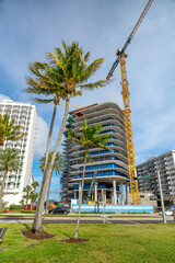 Naklejka premium Construction site of luxury condominium with yellow tower crane. High-rise building development with glass facade and palm trees in Miami USA