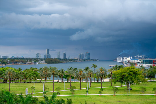 Dark storm clouds over Port of Miami and bay. Distant view of South Beach skyline and cruise ships at port under a heavy grey sky with green park foreground.