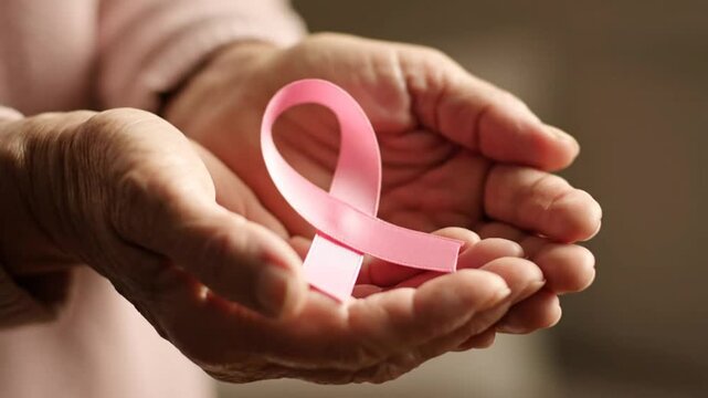 Elderly hands holding a pink ribbon, a symbol for breast cancer awareness and support