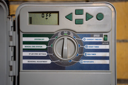 Close-up of irrigation controller panel showing time setting on digital display, selector dial, and buttons for automatic watering system.