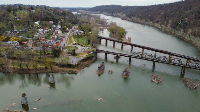 Harpers Ferry sits at Potomac&ndash;Shenandoah junction with rail bridges, steep streets, church ridge anchoring Lower Town. Brick blocks, budding trees, valley haze blend layered spring textures, WV