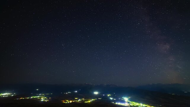 starry night time-lapse with mountains and settlement in foreground.