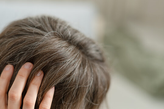 A woman notices hair loss along with graying strands on her head. The mature adult worries about thinning and shedding simultaneously. Mother faces multiple aging signs affecting hair density.