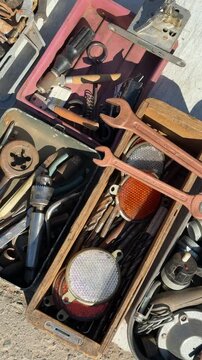 Secondhand tools on asphalt flea market, rusty pliers, wrenches, drill bits, wire cutters and sockets arranged in worn wooden