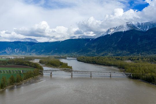 Scenic Fraser River Bridge Over Wide River With Snow-Capped Mountains and Cloudy Sky in British Columbia