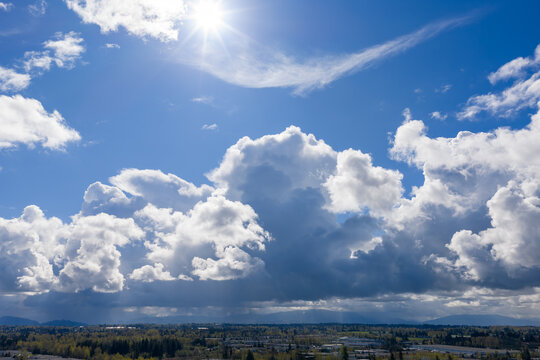 Dramatic Blue Sky With Sun and Towering Cumulus Clouds Over British Columbia Landscape
