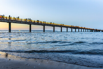 Obraz premium Long sea pier in evening twilight. Waves on foreground during sunset at the beach.