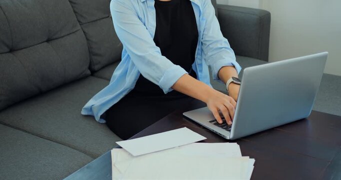 Individual arranging documents on coffee table. Person focused on sorting invoices and records at home. Home office scene showing person meticulously organizing paperwork and invoices on desk