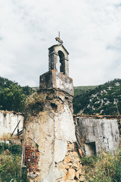 Weathered ruined bell tower with crumbling plaster, exposed brick and wild grass, standing in abandoned rural building against green mountain landscape