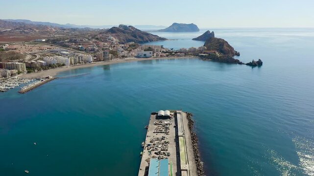 Aerial view of Aguilas city in Murcia, Spain, featuring Levante Bay and marina. Coastal urban landscape with calm Mediterranean waters, harbor structures and scenic shoreline.
