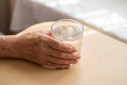 Senior woman hand with a subtle tremor holding a clear water glass