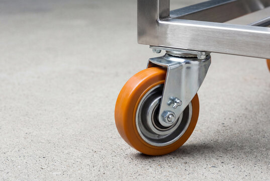 Orange industrial caster wheel on a metal trolley for moving heavy equipment